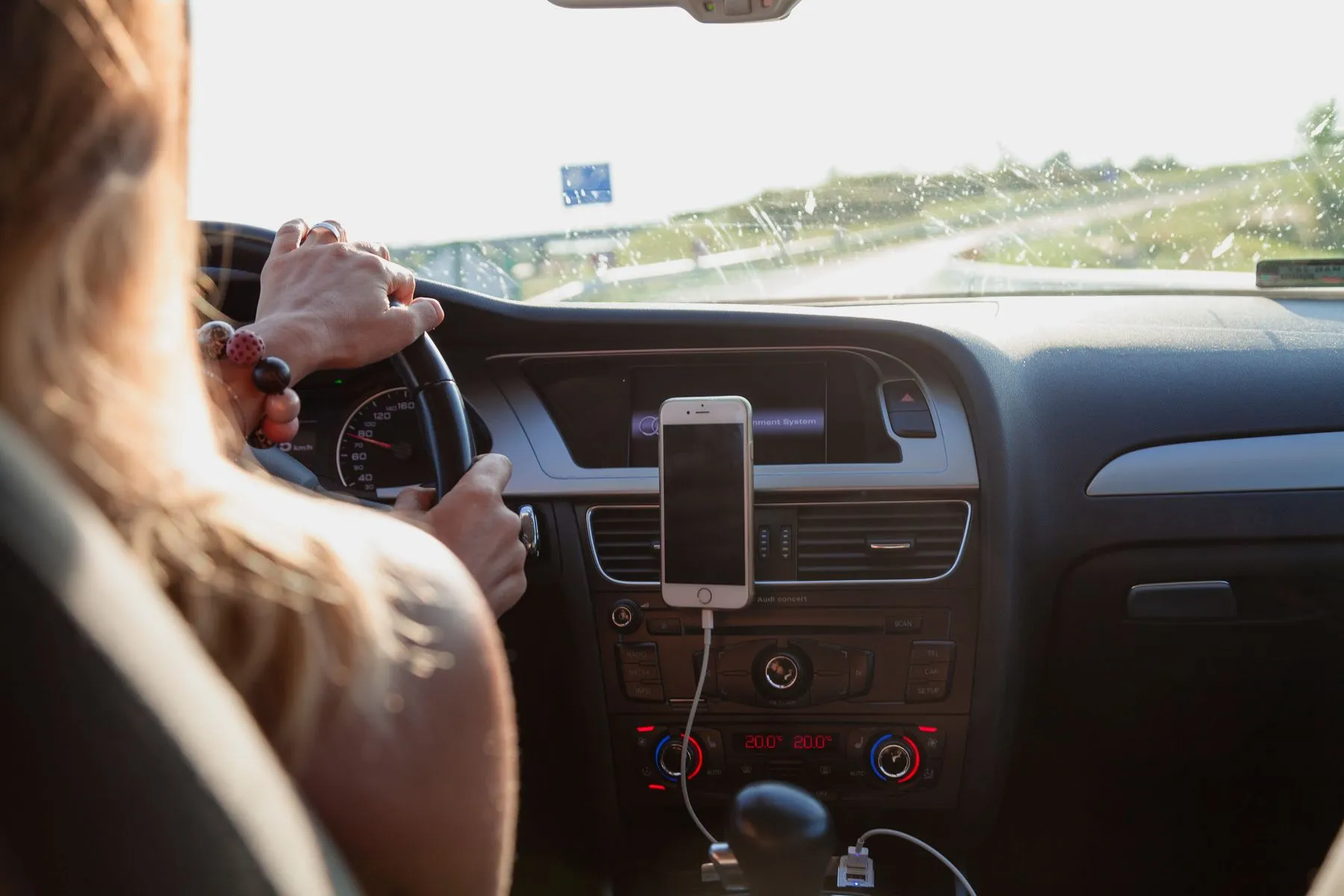 A driver at the wheel with a phone mounted on the dashboard showing navigation, as used for a HeyGo trip